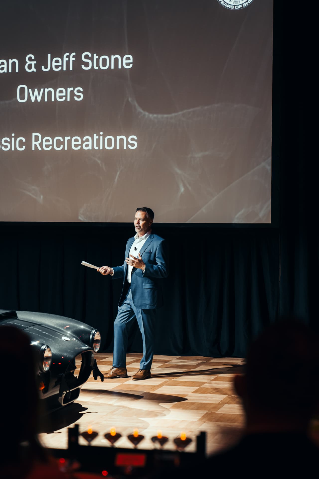 Owner presenting on stage beside a Shelby Cobra
