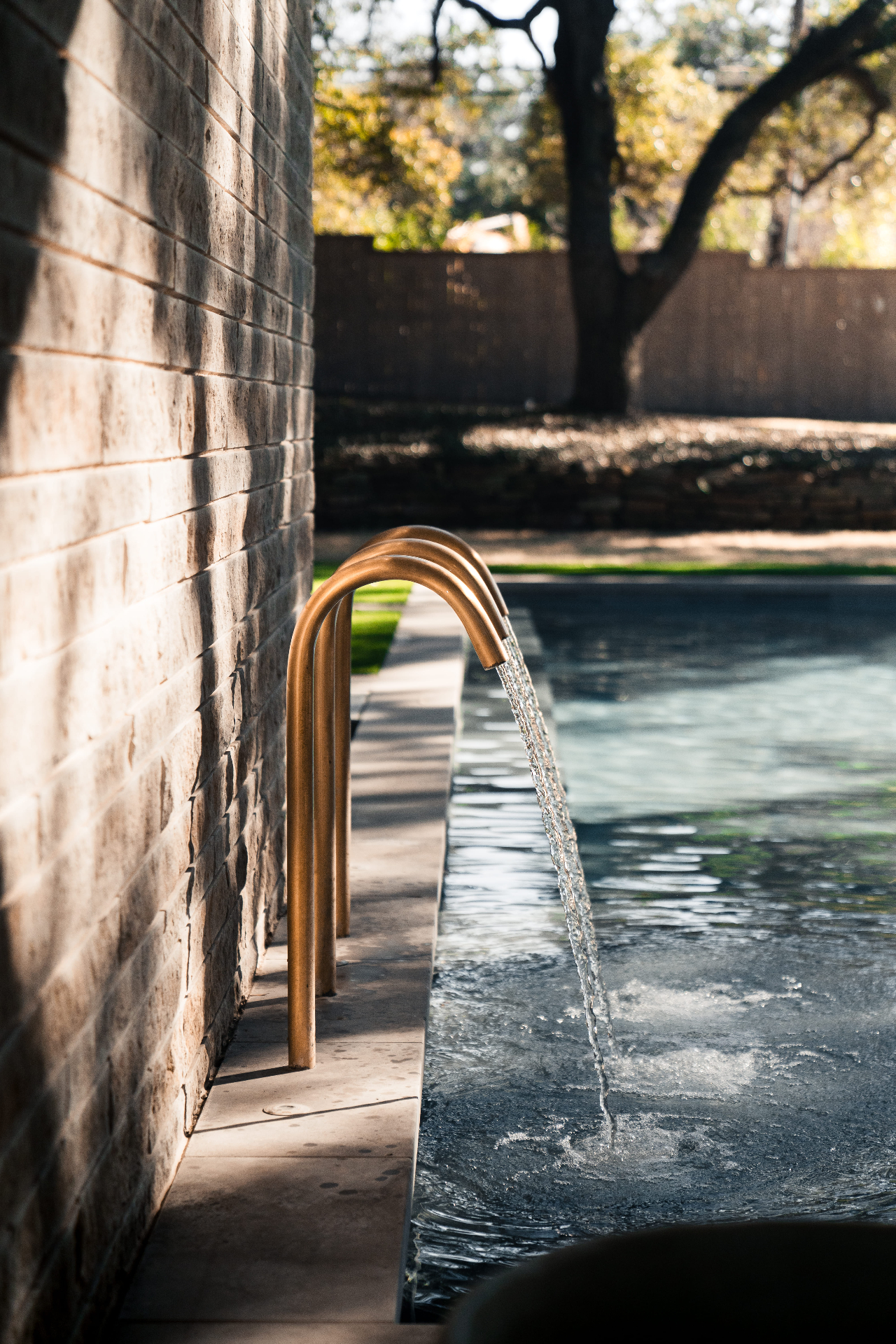 Bronze pool spouts flowing into water beside stone wall