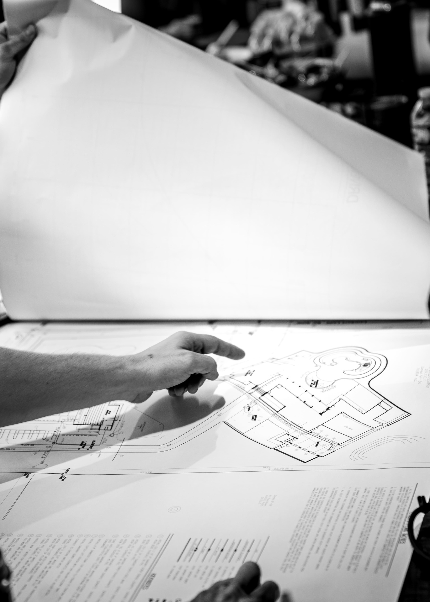 Hand pointing at blueprint detail in black and white