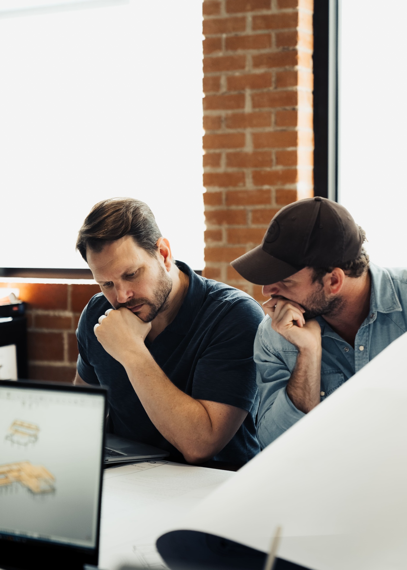 Two team members reviewing plans by brick window